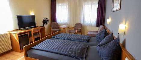 A hotel room with a bed, a desk, a television, a fan, and a window with curtains.