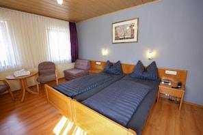 A hotel room with two beds, a desk, a chair, and a window with curtains. - Hotel Kambeitz (Ötigheim)