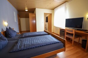 Quarto com duas camas, televisão, escrivaninha e espelho.