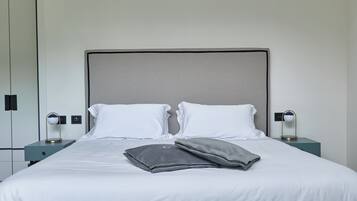 A neatly made bed with two pillows, a bedside table with a lamp, and a wall-mounted switch.