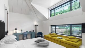 Habitació d'hotel moderna amb llit, escriptori, sofà i finestres grans.