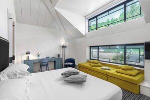 A modern hotel room with a bed, a desk, a sofa, and large windows.