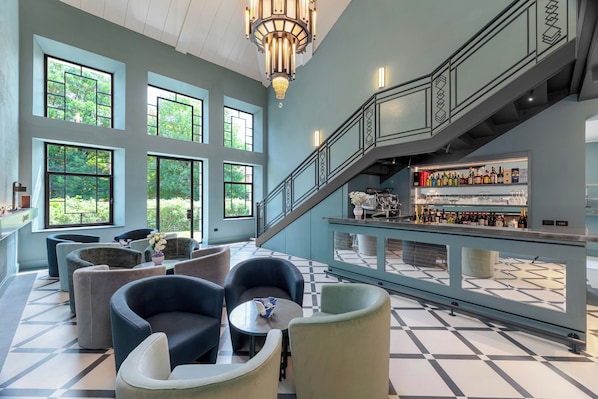 A spacious lobby with multiple seating areas, a staircase, and a bar with a wine selection.