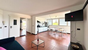 A living room with a sofa, a coffee table, and a TV mounted on the wall. - Stunning penthouse with a sun terrace in the center of Lignano, 150 meters from the sea (Lignano Sabbiadoro)