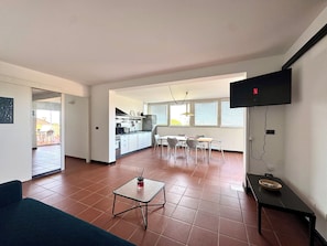 Un saló modern amb un sofà, una taula petita, un televisor penjat a la paret i una cuina al fons.