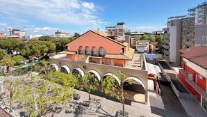 A multi-story building with a red facade, a courtyard with trees, and a clear blue sky. - Stunning penthouse with a sun terrace in the center of Lignano, 150 meters from the sea (Lignano Sabbiadoro)