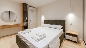 A modern hotel room with a large bed, a bedside table, a mirror, and an open door leading to a bathroom. - A H Azure Apartaments 1BR (Vlorë)