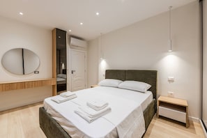 Ein modernes Hotelzimmer mit einem großen Bett, einem Nachttisch, einem Spiegel und einer offenen Tür zu einem Badezimmer.