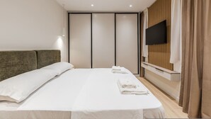 A modern hotel room with a large bed, a flat-screen TV mounted on the wall, and a sliding door closet. - A H Azure Apartaments 1BR (Vlorë)