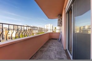 Ein Balkon mit Metallgeländer, einer Schiebetür aus Glas und Blick auf Gebäude im Hintergrund.