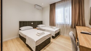 Ein Hotelzimmer mit zwei Betten, einem Schreibtisch, einem Stuhl und einem großen Fenster mit Vorhängen.