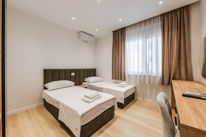 Ein Hotelzimmer mit zwei Betten, einem Schreibtisch, einem Stuhl und einem großen Fenster mit Vorhängen.
