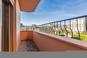 Ein Balkon mit Metallgeländer, ein klarer Himmel und Gebäude im Hintergrund.