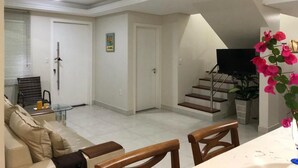 Un salon comprenant un canapé, des fauteuils, un téléviseur et un escalier menant à l’étage supérieur.