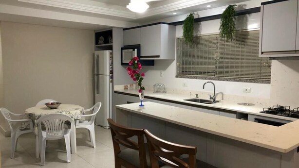 Une cuisine moderne avec un îlot central, des chaises blanches, un réfrigérateur et une fenêtre avec des stores.