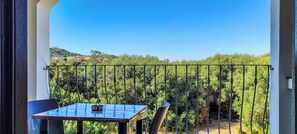 Ein Balkon mit Tisch und Stühlen, mit Blick auf einen Weinberg und entfernte Gebäude.