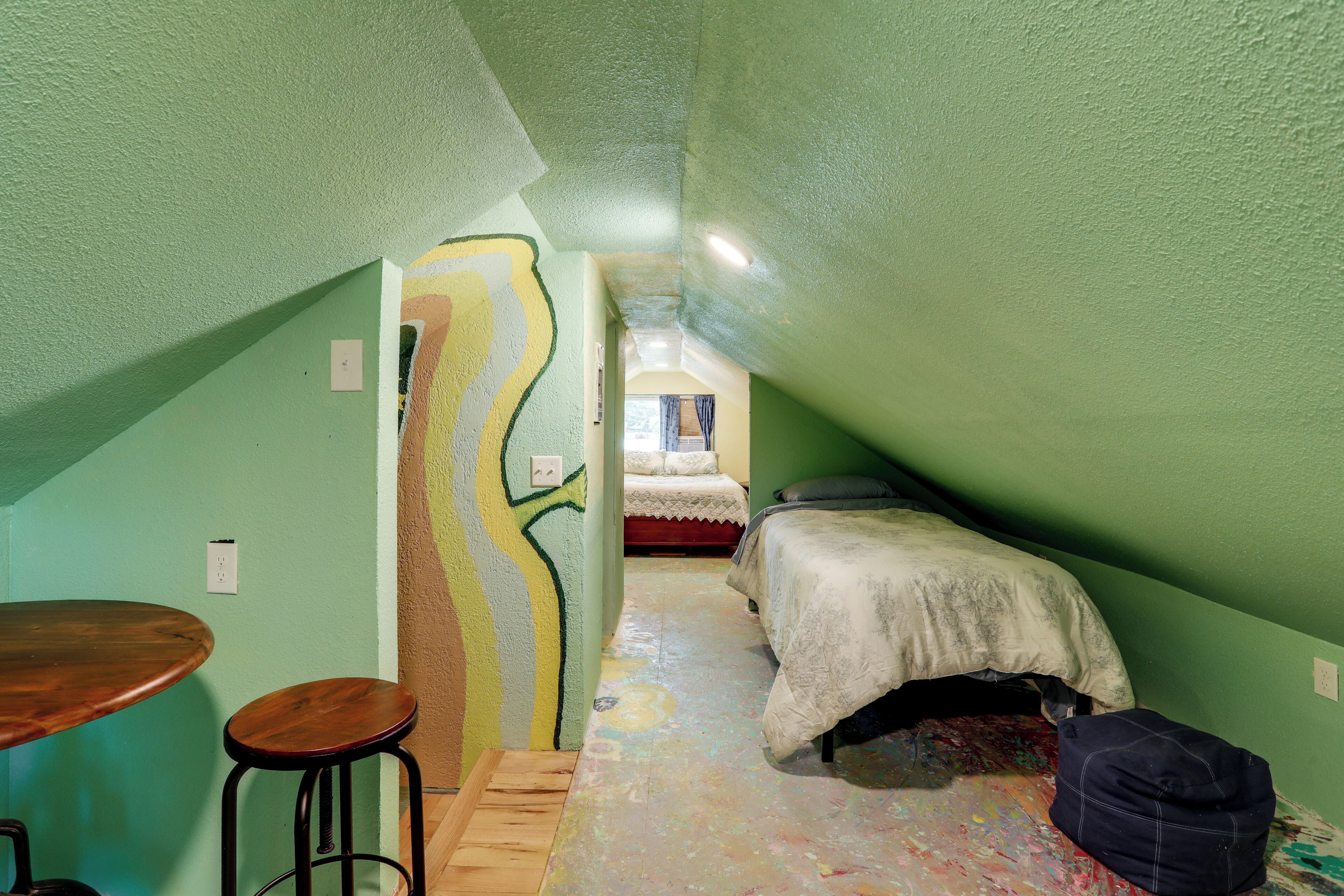 A narrow room with a bed, a table, and a stool.