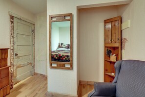 A room with a wooden door, a mirror, a blue chair, and a wooden cabinet. - Home Near Eleven Point River & Nat'l Forest! (Alton)