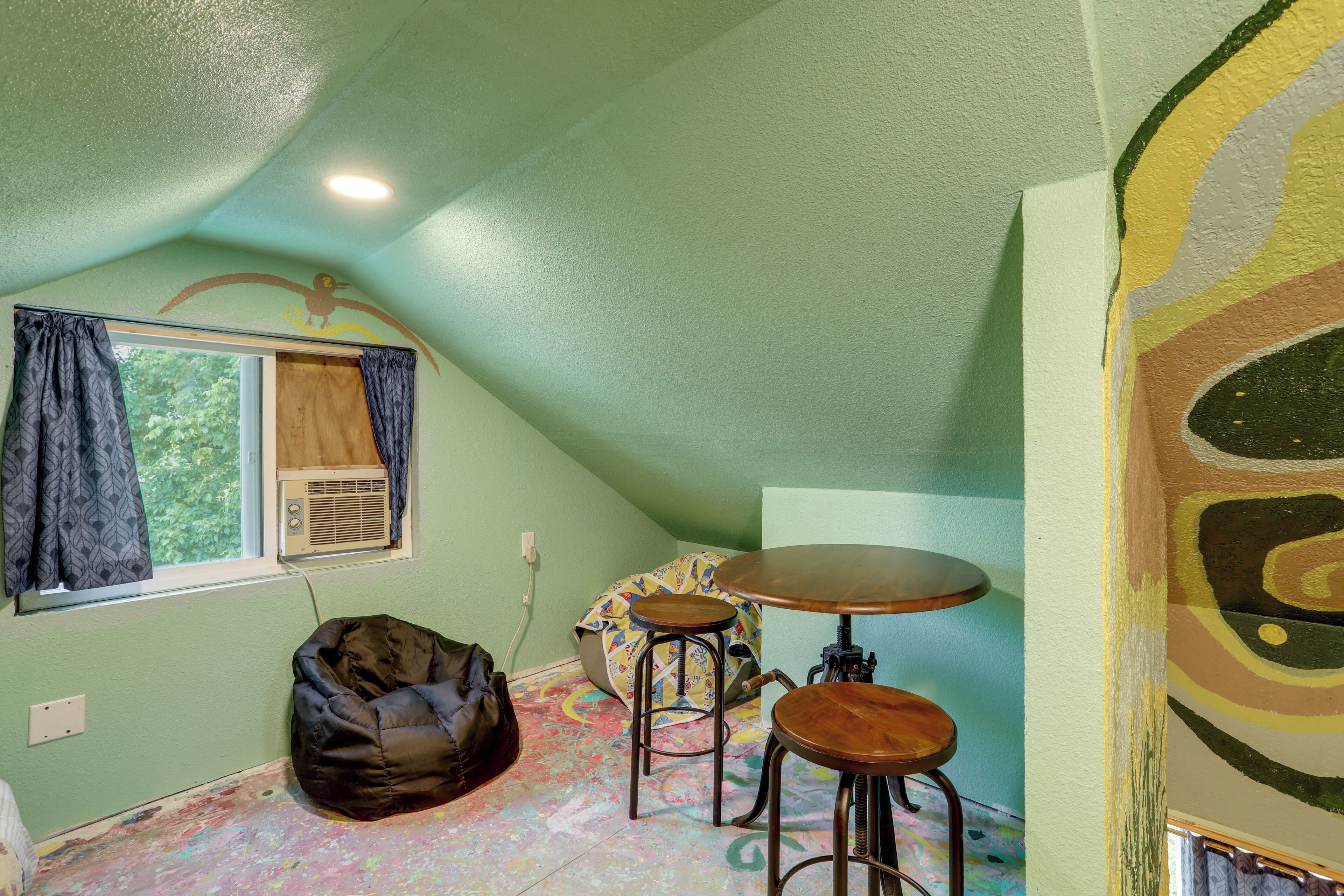A room with a sloped ceiling, a bean bag chair, a small table with stools, and a window with curtains.
