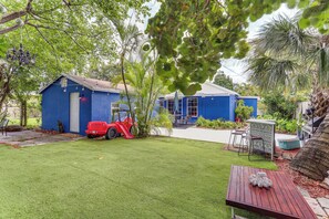 A blue house with a red tractor, a small table, and a garden with palm trees.