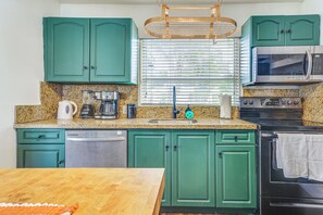 A kitchen with teal cabinets, a granite countertop, a coffee maker, a microwave, and a stove.