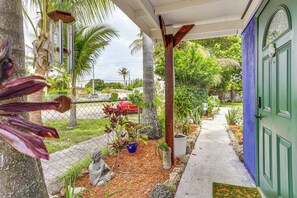 A porch with a green door, a statue, and various potted plants.