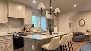 A modern kitchen with a central island, bar stools, a refrigerator, and a dining area with a sofa and side table.