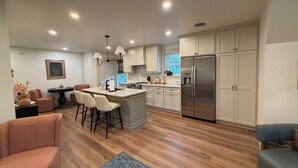 A modern kitchen with white cabinets, a stainless steel refrigerator, and a dining area with a table and chairs.