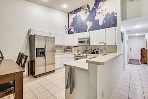 A modern kitchen with a stainless steel refrigerator, microwave, and oven, a world map on the wall, and a small island with a sink.
