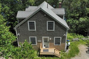 A two-story wooden house with a front porch, a visible door, and a small attached shed. - Waterfront Cottage! Family-friendly Hideaway (Round Pond)