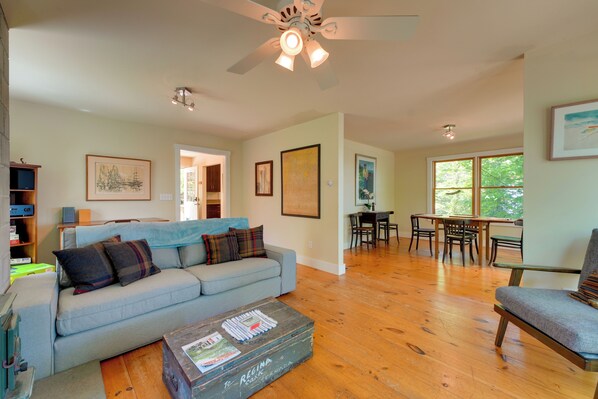 A living room with a sofa, a coffee table, a dining area with a table and chairs, and a ceiling fan. - Waterfront Cottage! Family-friendly Hideaway (Round Pond)