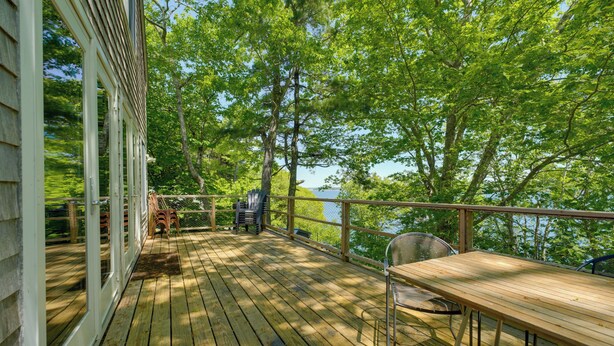A wooden deck with a table and chairs, overlooking a body of water and surrounded by trees. - Waterfront Cottage! Family-friendly Hideaway (Round Pond)