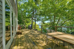 A wooden deck with a table and chairs, overlooking a body of water and surrounded by trees. - Waterfront Cottage! Family-friendly Hideaway (Round Pond)