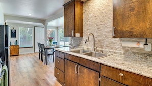 A kitchen with wooden cabinets, a granite countertop, a stainless steel sink, and a brick backsplash. - Walk to Spanaway Lake: Chic Home w/ Rooftop Deck! (Spanaway)