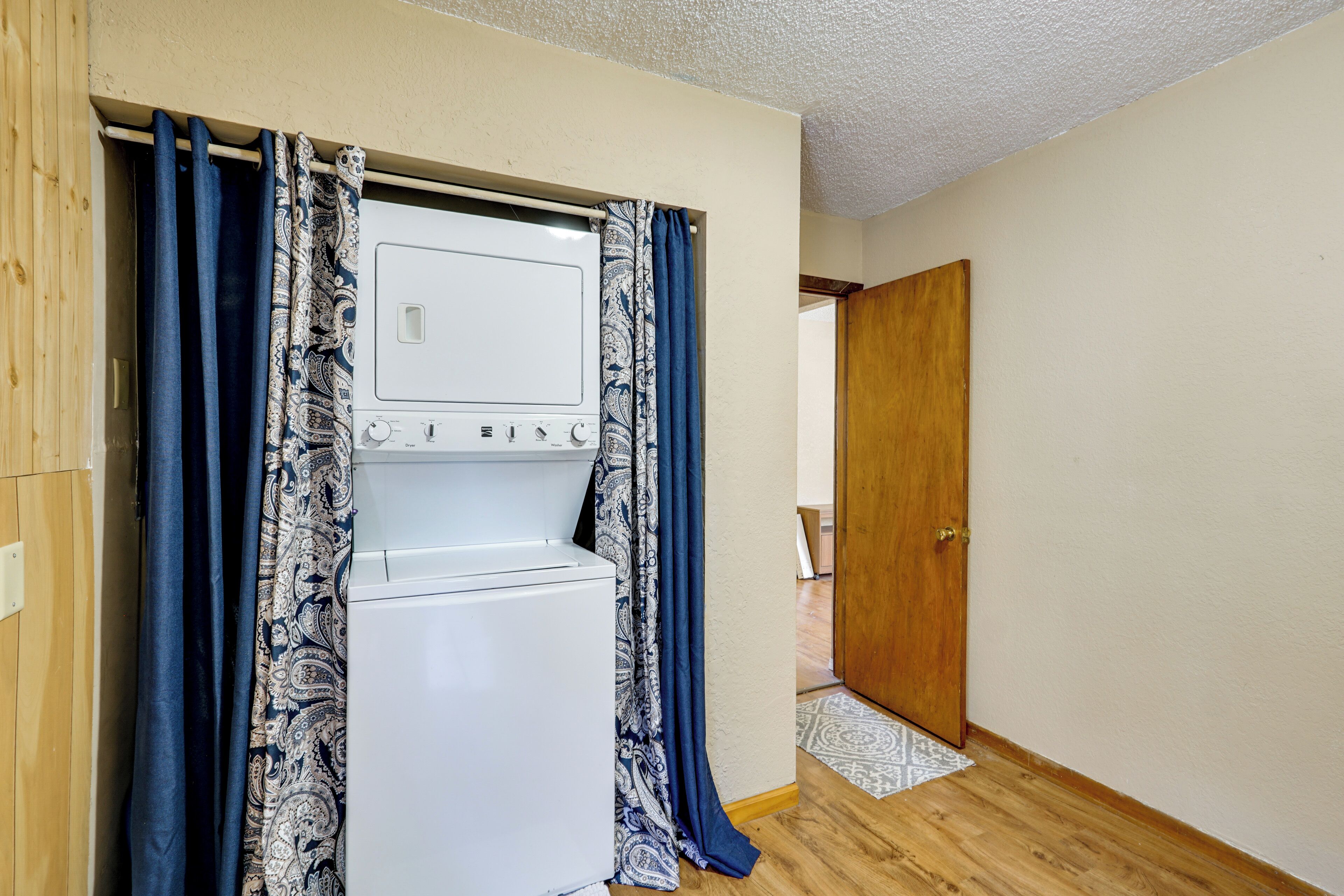 Une buanderie avec un lave-linge et un sèche-linge blancs, des rideaux à motifs et une porte en bois.