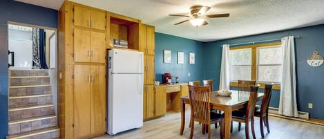 A kitchen with wooden cabinets, a refrigerator, a dining table with chairs, and a ceiling fan.