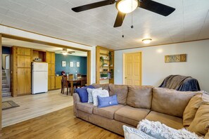 A living room with a brown sofa, a ceiling fan, and a dining area in the background.