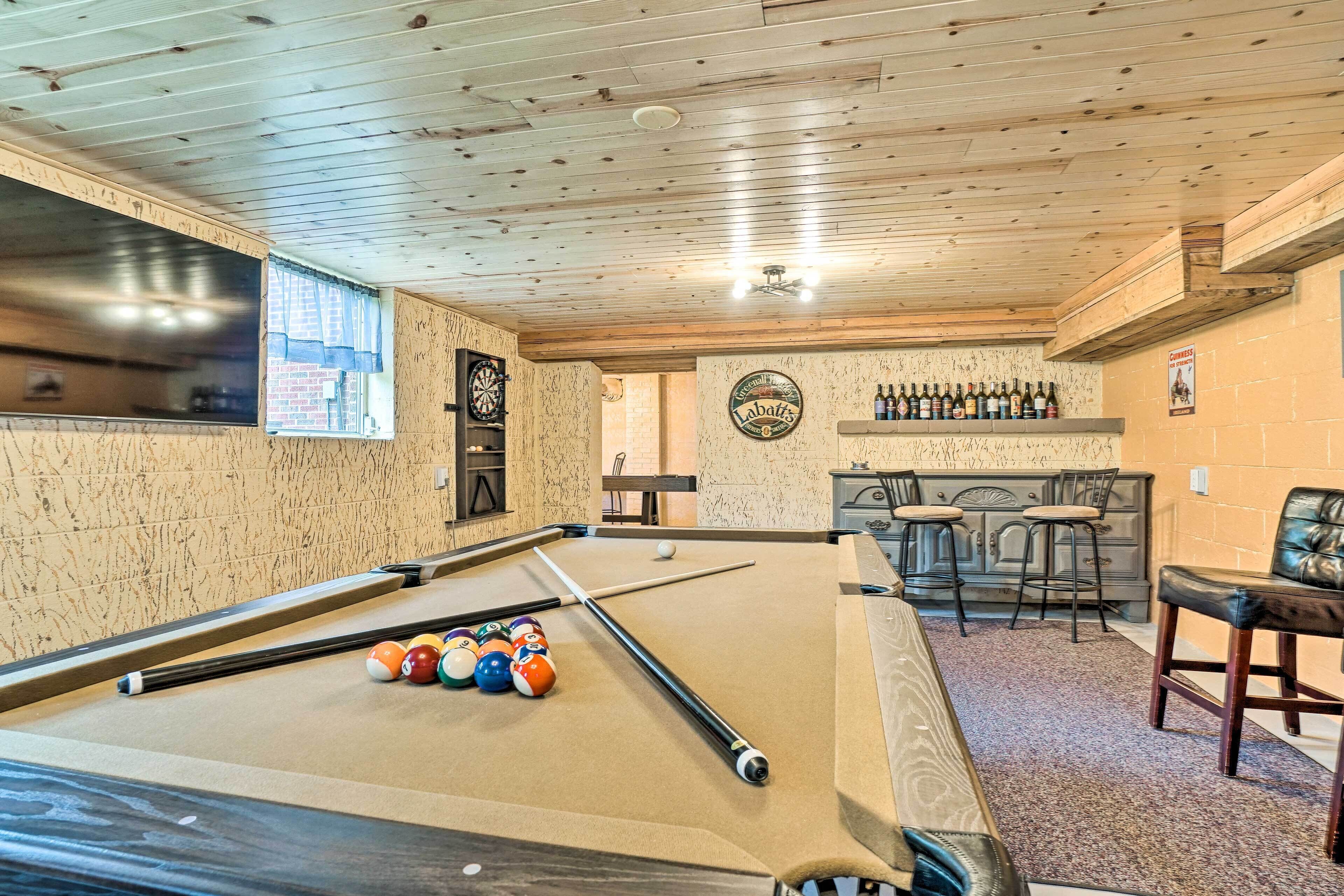 A pool table with billiard balls, a dartboard, and a bar area with stools.