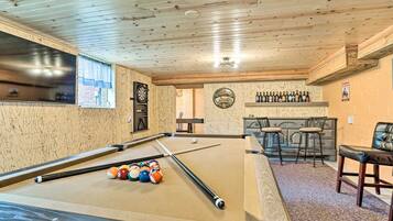 A pool table with billiard balls, a dartboard, and a bar area with stools.