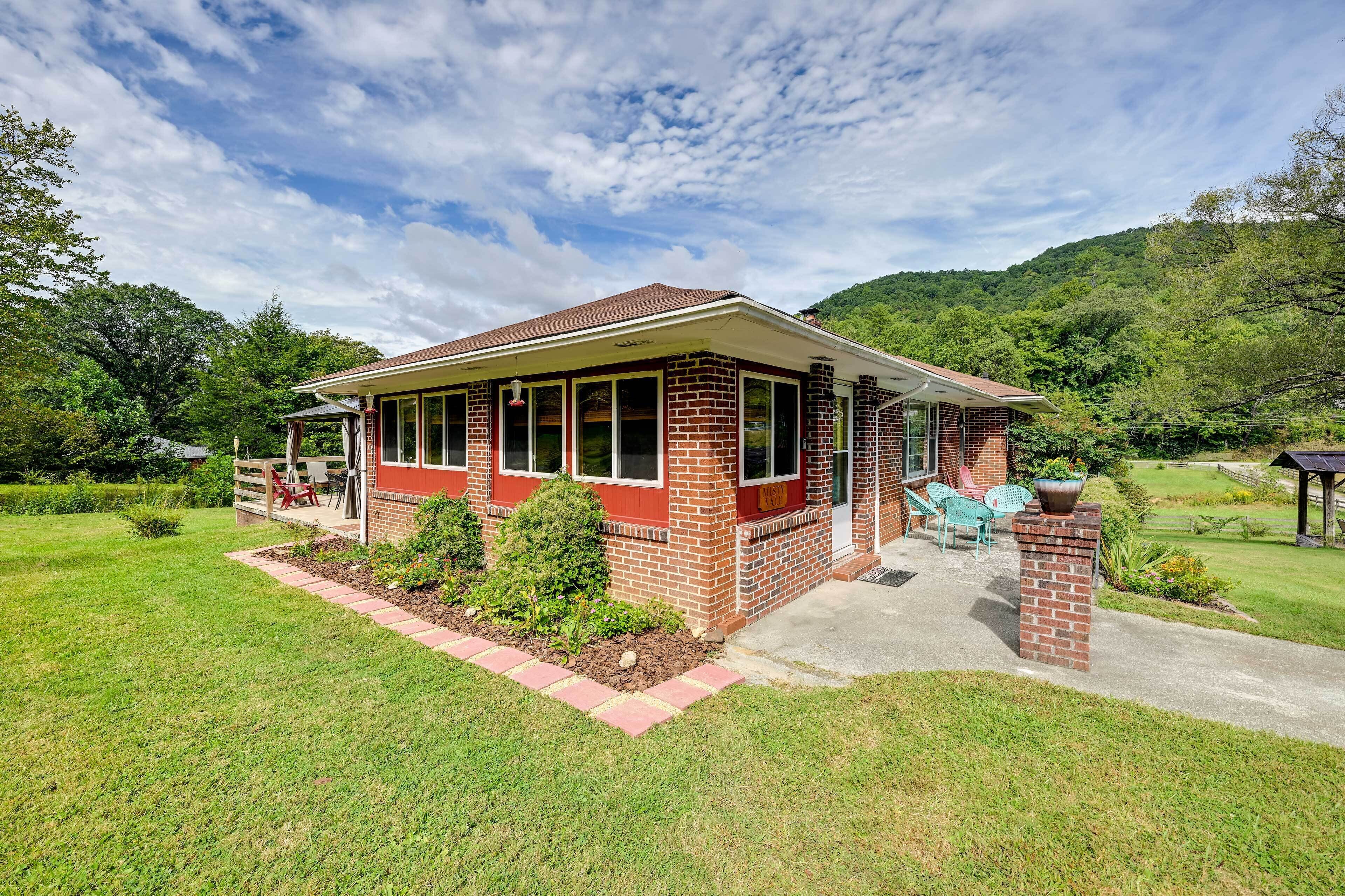 A single-story brick house with a covered porch, a small garden, and a view of a hilly landscape.