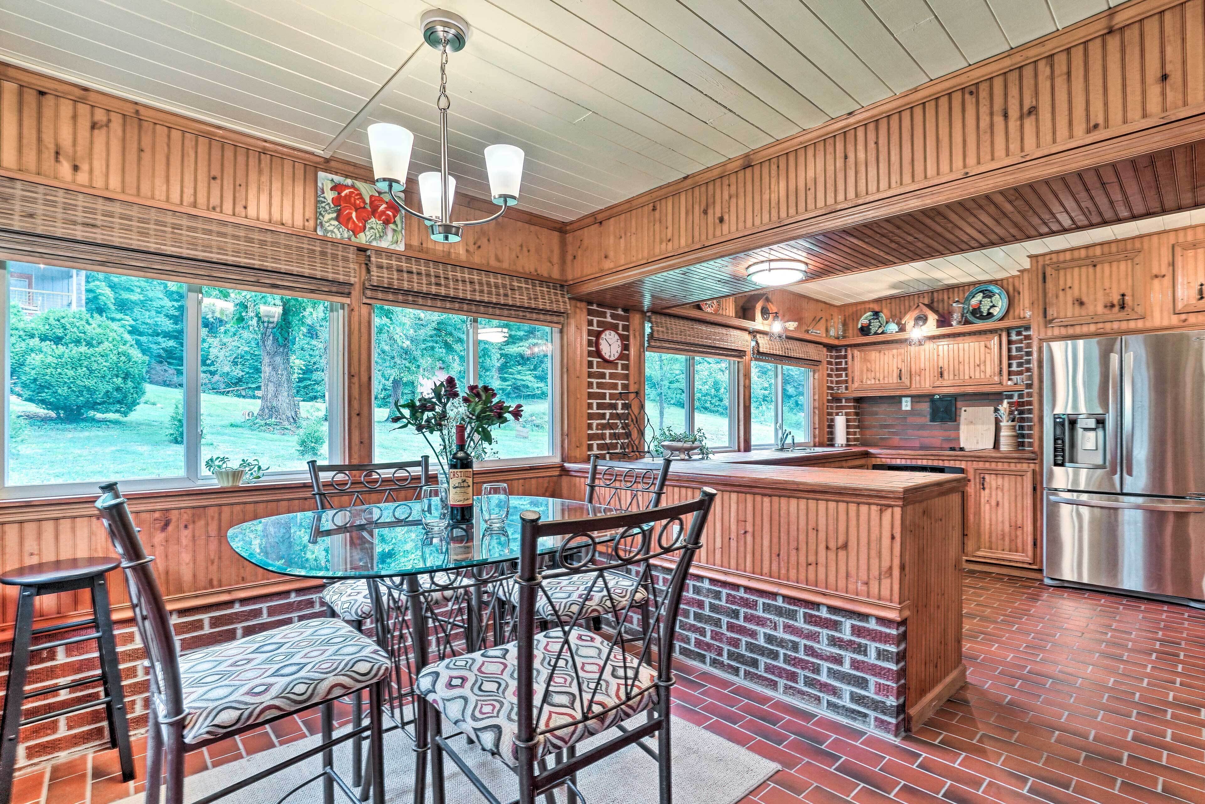 A kitchen with a brick floor, wooden cabinets, a stainless steel refrigerator, and a dining area with a glass table and chairs.