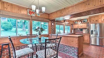 A kitchen with a brick floor, wooden cabinets, a stainless steel refrigerator, and a dining area with a glass table and chairs.