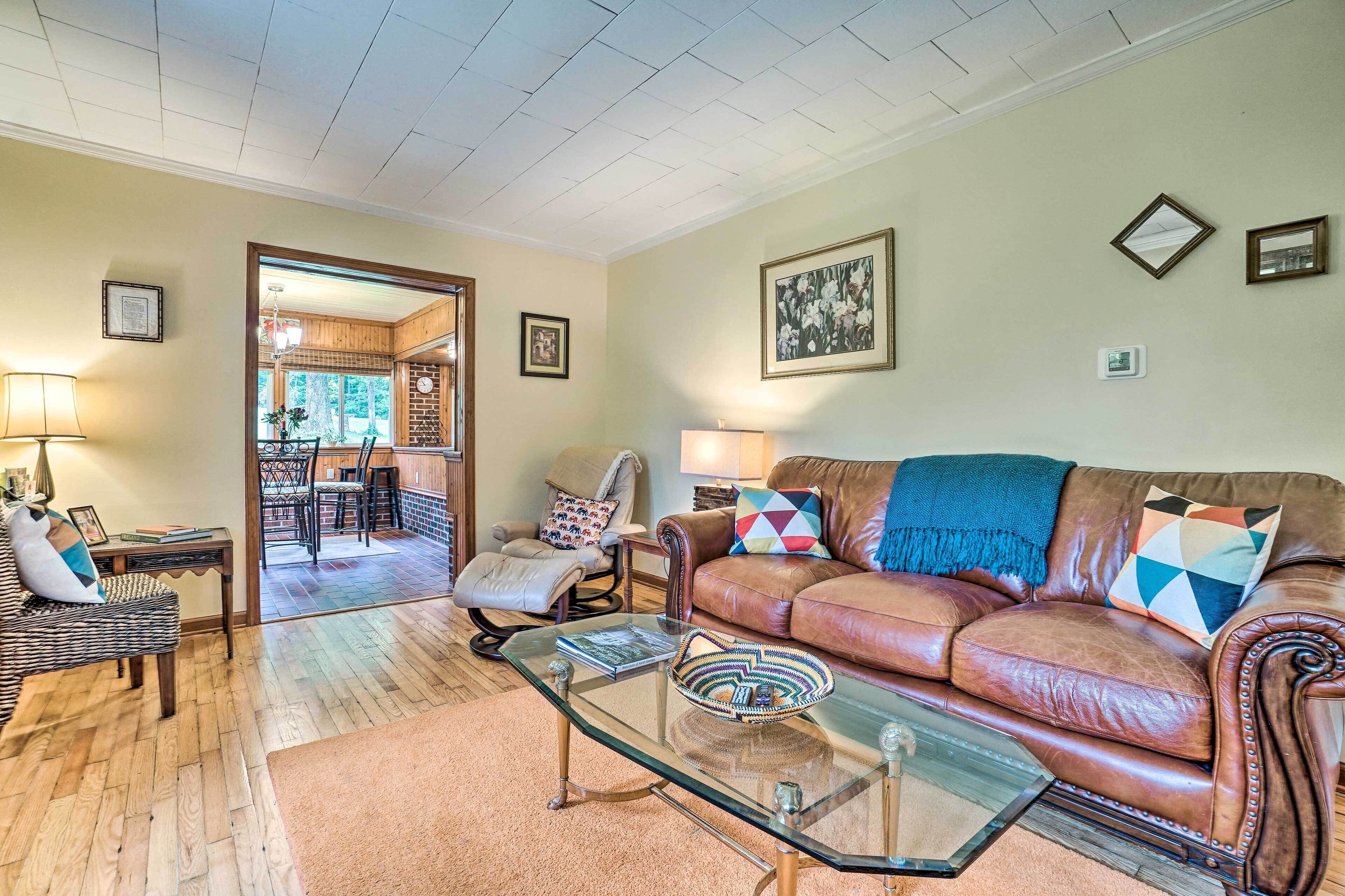 A living room with a brown leather sofa, glass coffee table, and a dining area with a wooden table and chairs.
