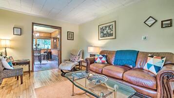 A living room with a brown leather sofa, glass coffee table, and a dining area with a wooden table and chairs.