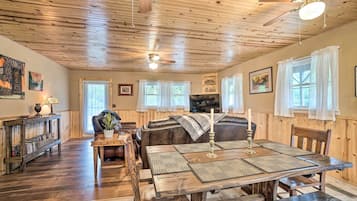 A cozy room with a wooden ceiling, a dining table with placemats, a leather sofa, and a bookshelf.