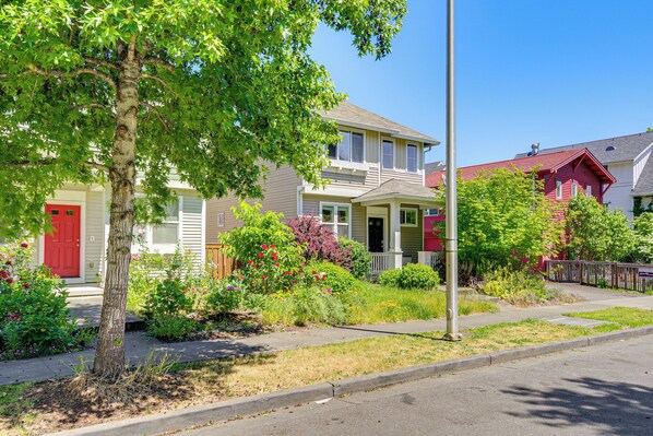 A residential street with houses, a sidewalk, and a tree.