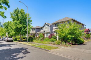 A residential street with houses, parked cars, and lush greenery.