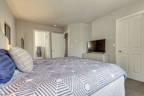 Une chambre à coucher avec un lit, un téléviseur posé sur une commode et une porte donnant sur une autre pièce.
