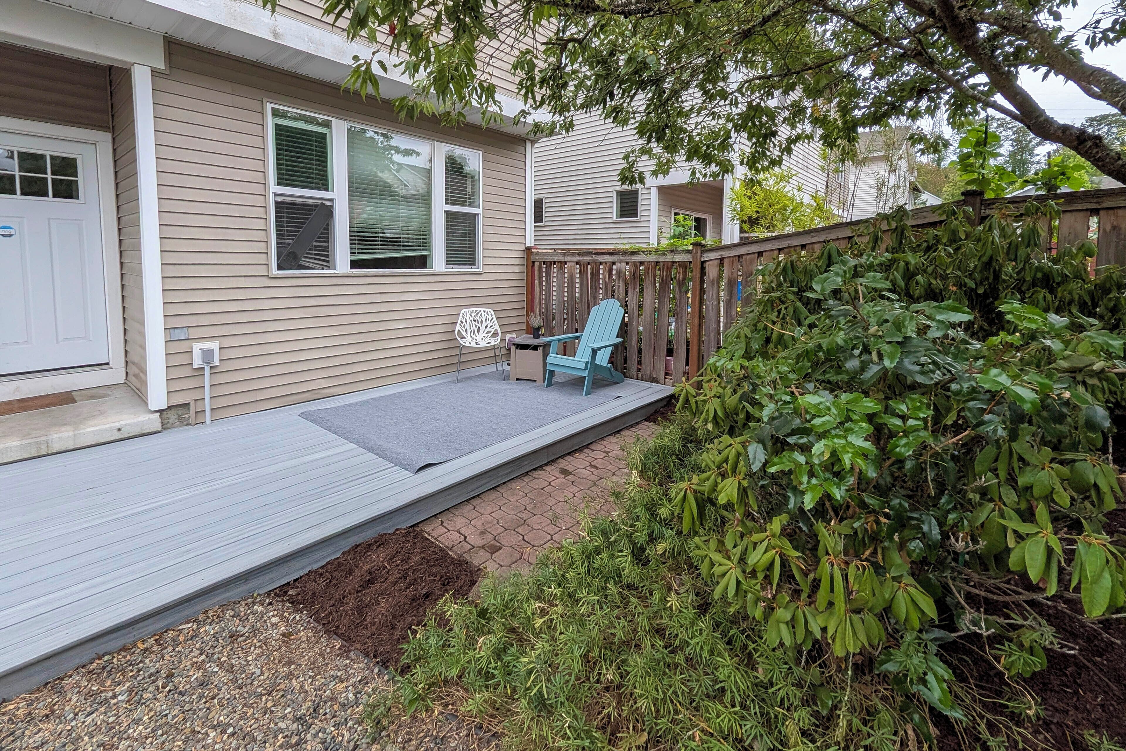 A residential deck with a blue chair, a small garden area with mulch and plants, and a wooden fence.
