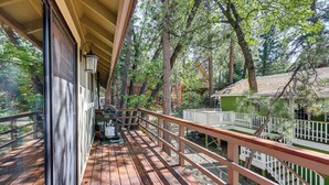A wooden deck with a railing, a glass door, and a view of trees and a building. - 2 Mi to Big Bear Lake! Family Haven w/ Hot Tub (Big Bear City)